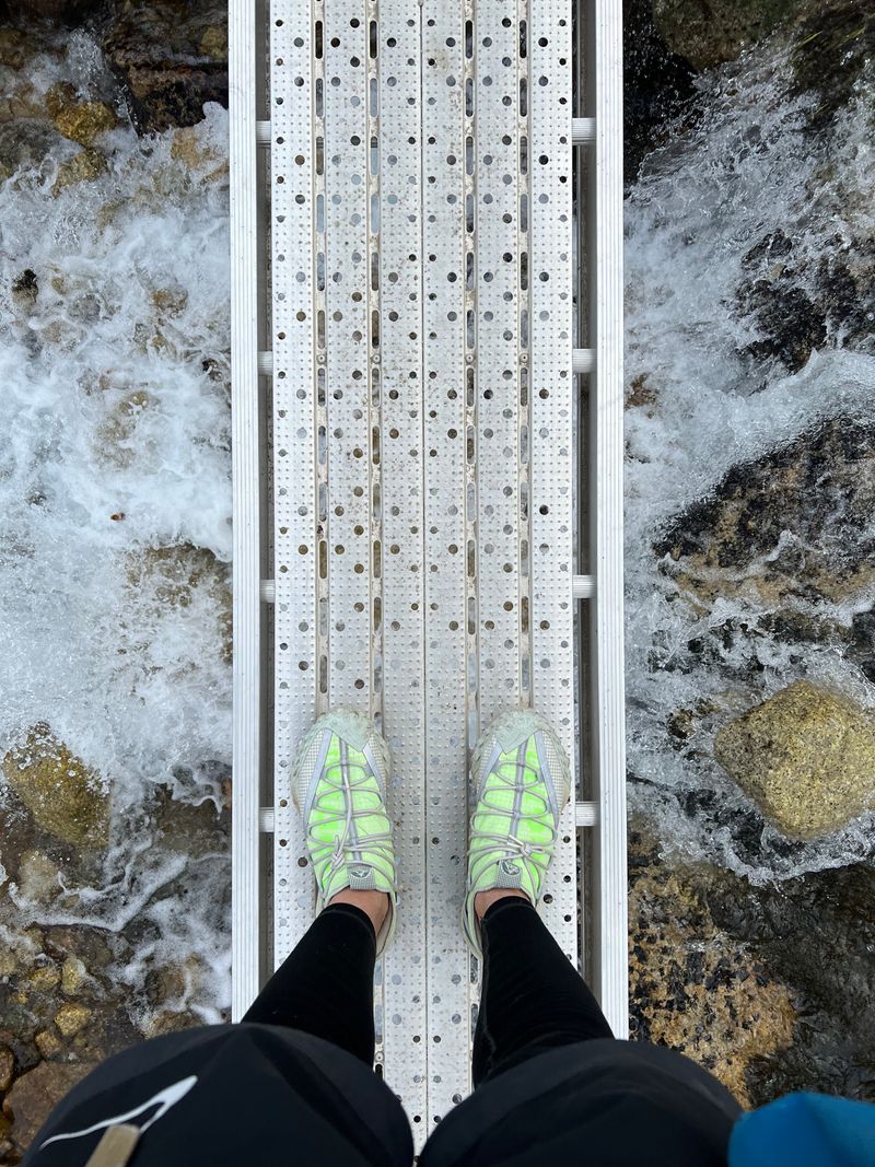 Admiring my shoes on a narrow bridge above a rapid creek.